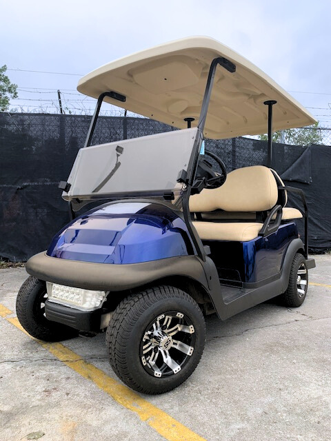 A stylish blue golf cart with a beige top and comfortable seating, parked on a concrete surface.